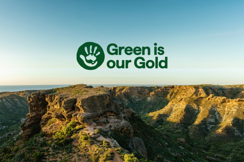 Green is our Gold logo, featuring a handprint with the map of Australia, over a sun-drenched landscape of rugged rocky ridges and deep canyons at Cape Range National Park, Exmouth, highlighting the region's natural beauty. © Tourism Australia