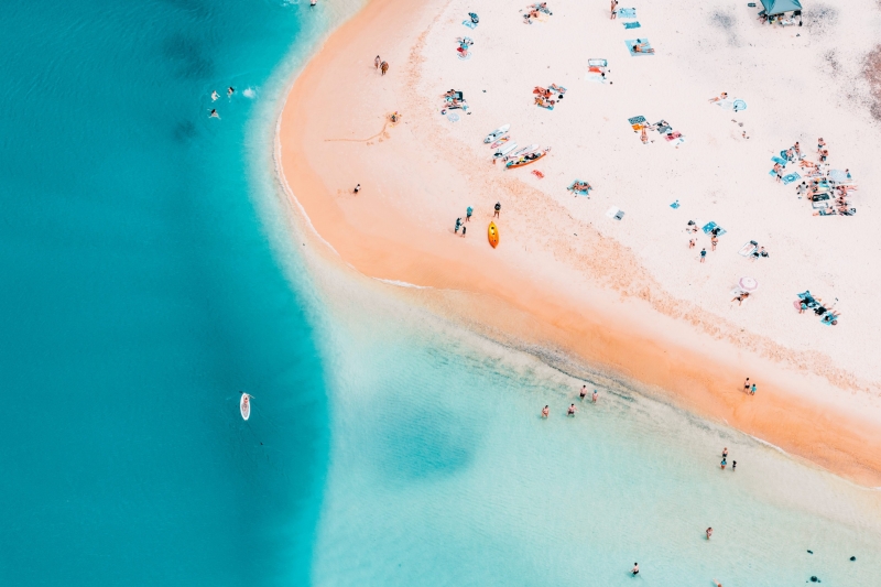 Aerial view of Currumbin Beach, nestled on the stunning Gold Coast of Queensland. Crystal-clear blue waters meet the sandy shore, where beachgoers enjoy a refreshing swim. The scene is vibrant with people frolicking in the inviting waves, creating a picturesque summer setting © Tourism Australia