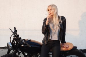 Sexy fashion female biker girl. Young woman sitting on vintage motorcycle and smoking cigarette. Outdoors lifestyle portrait